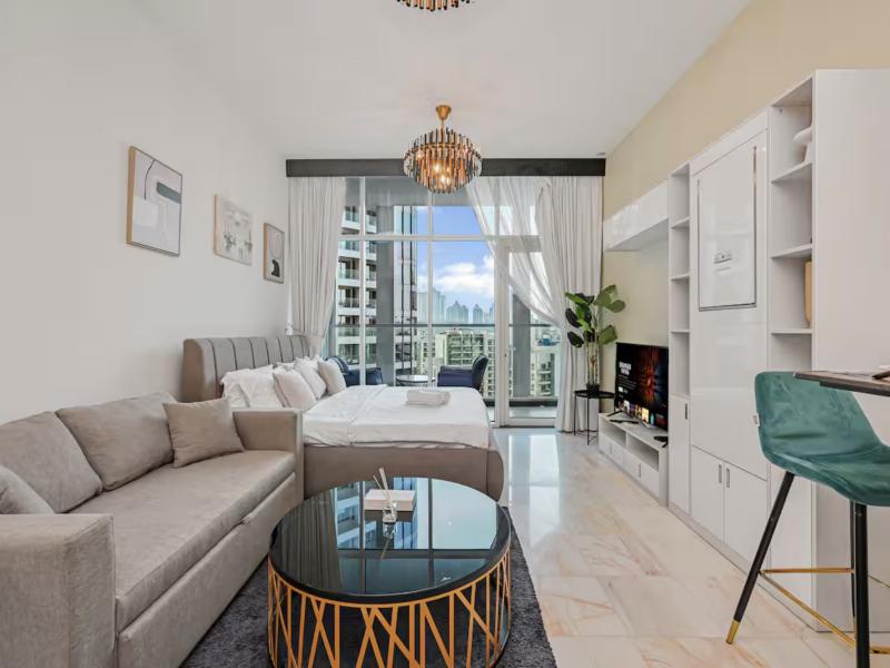 Studio living area with sofa, bed, chandelier and balcony doors